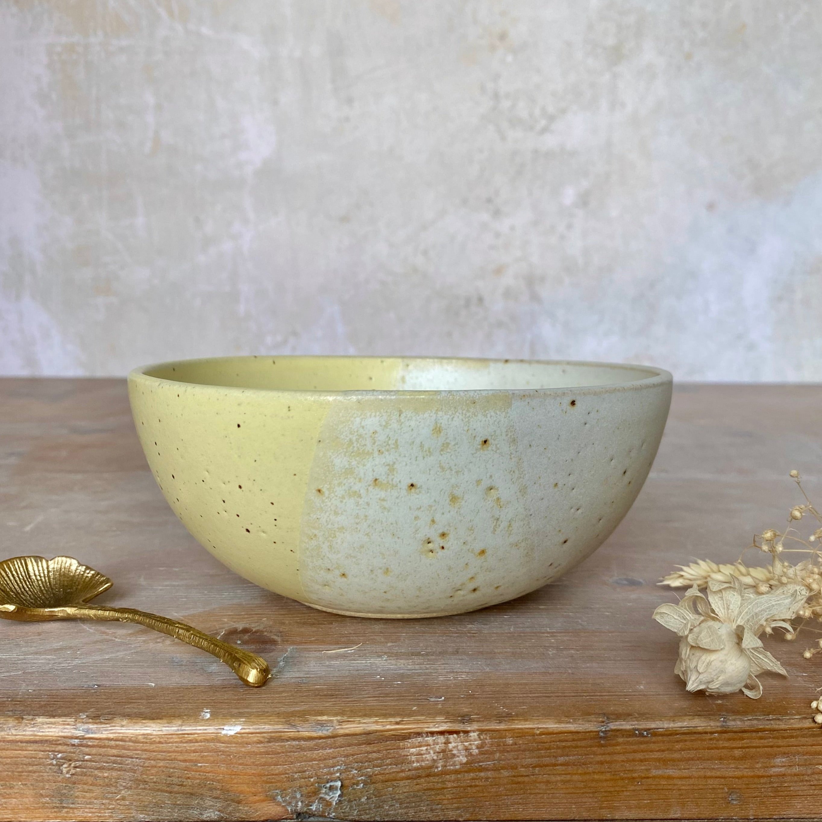 Speckled ceramic bowl, half pale yellow, half off-white.  The bowl has a rounded shape and a slightly speckled texture.