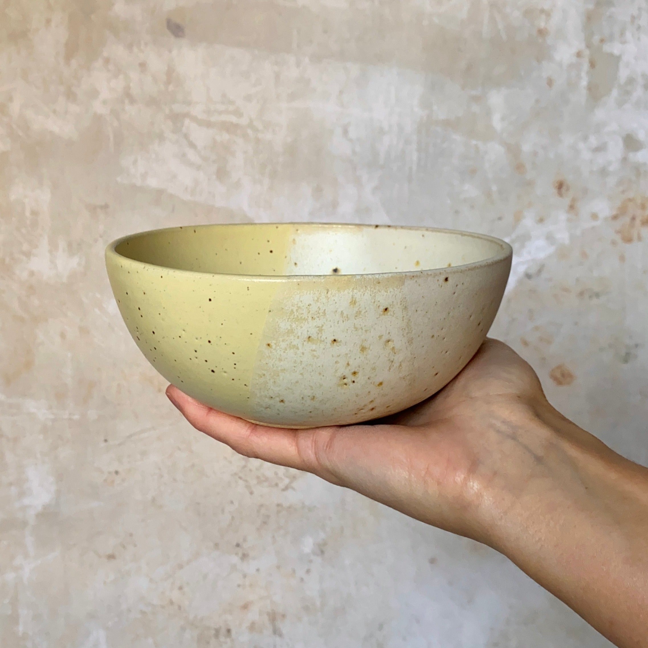 Hand-held ceramic bowl with speckled, two-toned glaze in pale yellow and off-white.