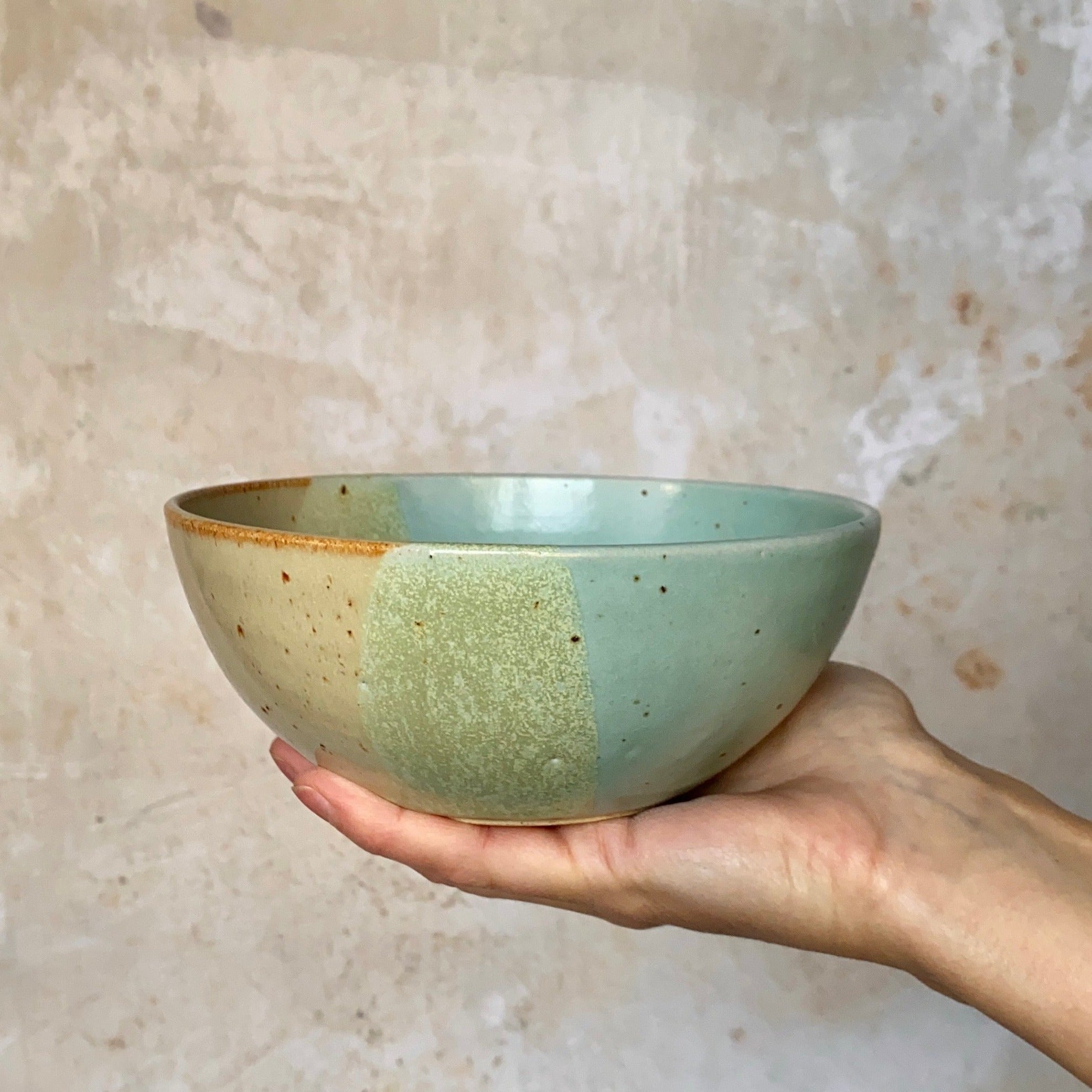 Hand-held ceramic bowl with speckled, two-toned glaze in pale green and beige.