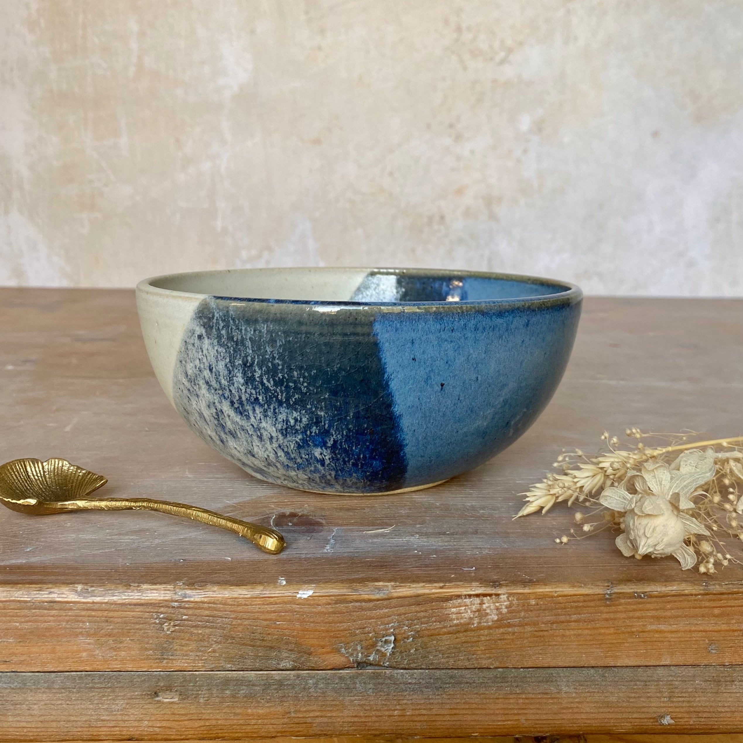 Hand-thrown ceramic bowl with speckled off-white and blue glaze, showing a mottled, uneven application of color.