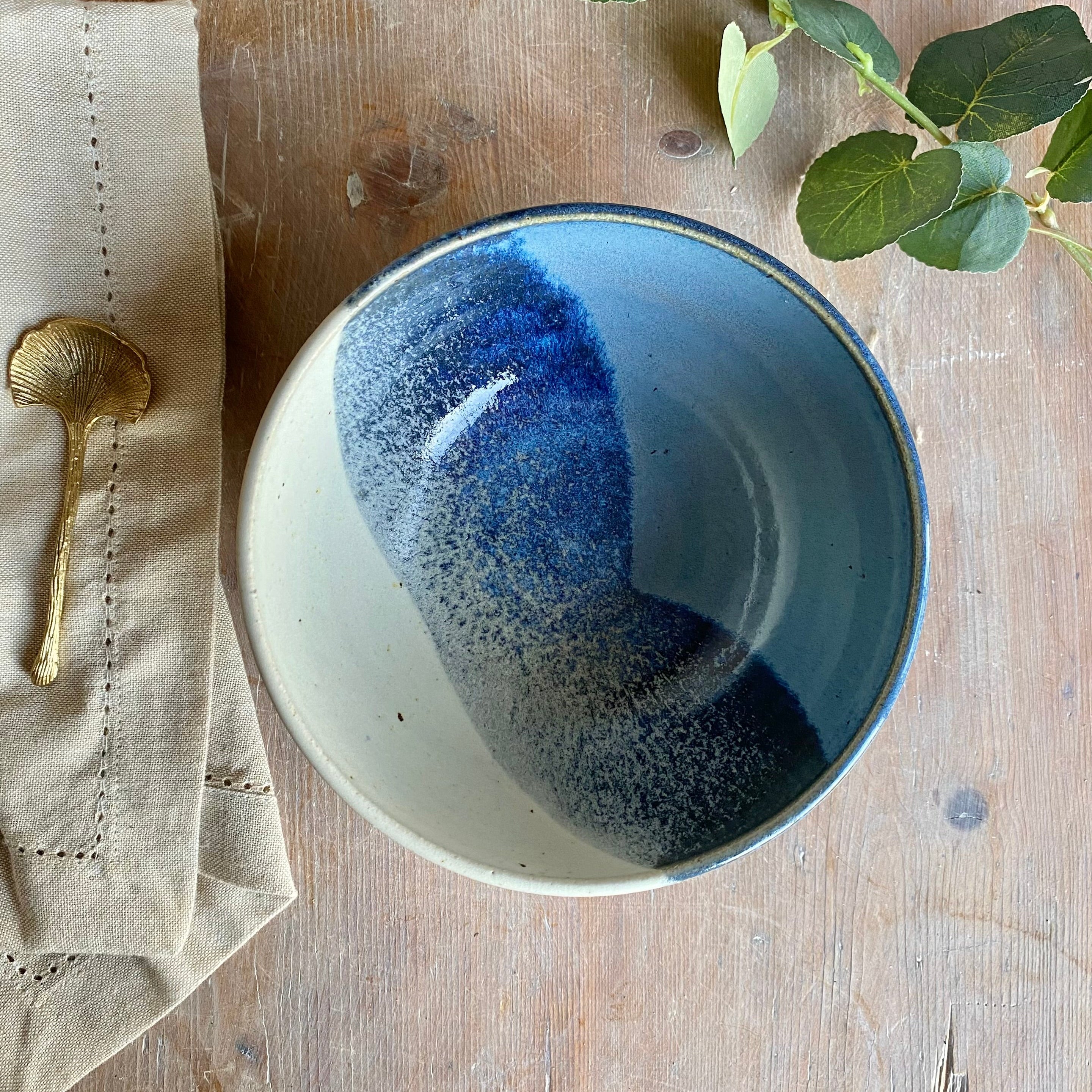 Handcrafted ceramic bowl with a speckled, two-toned glaze in shades of blue and off-white.  The bowl has a dark rim.