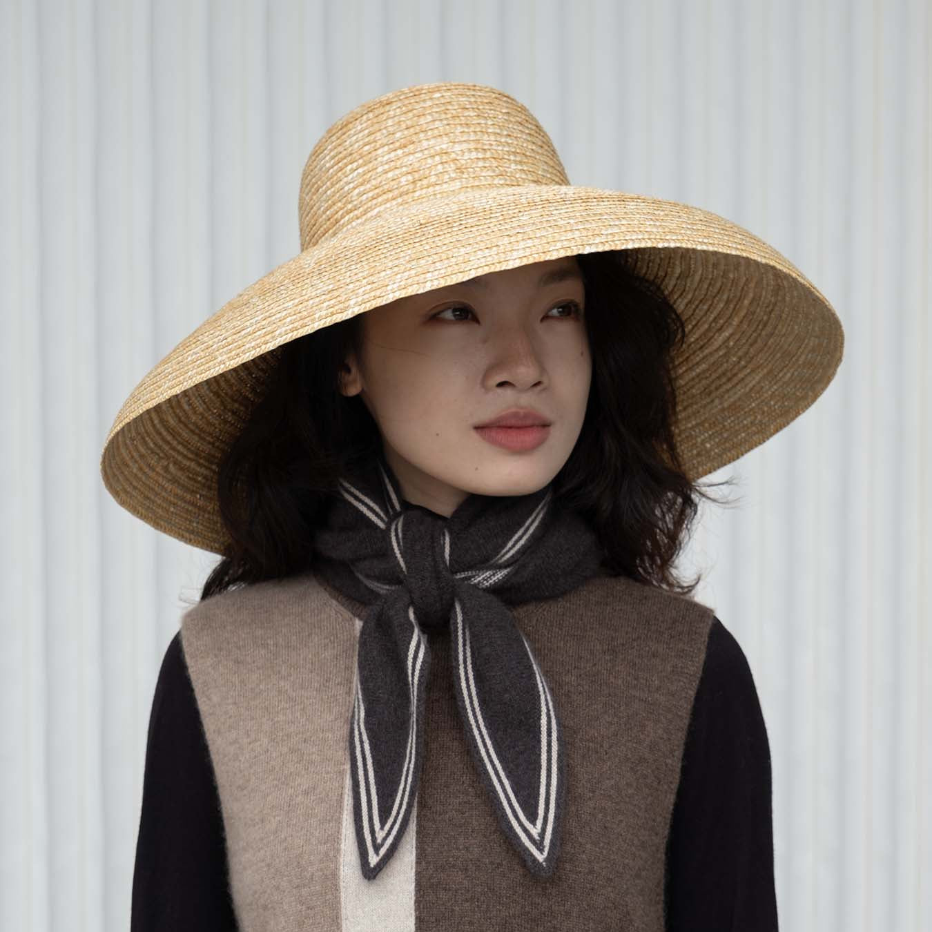 Woman wearing a straw hat and a striped scarf against a white background