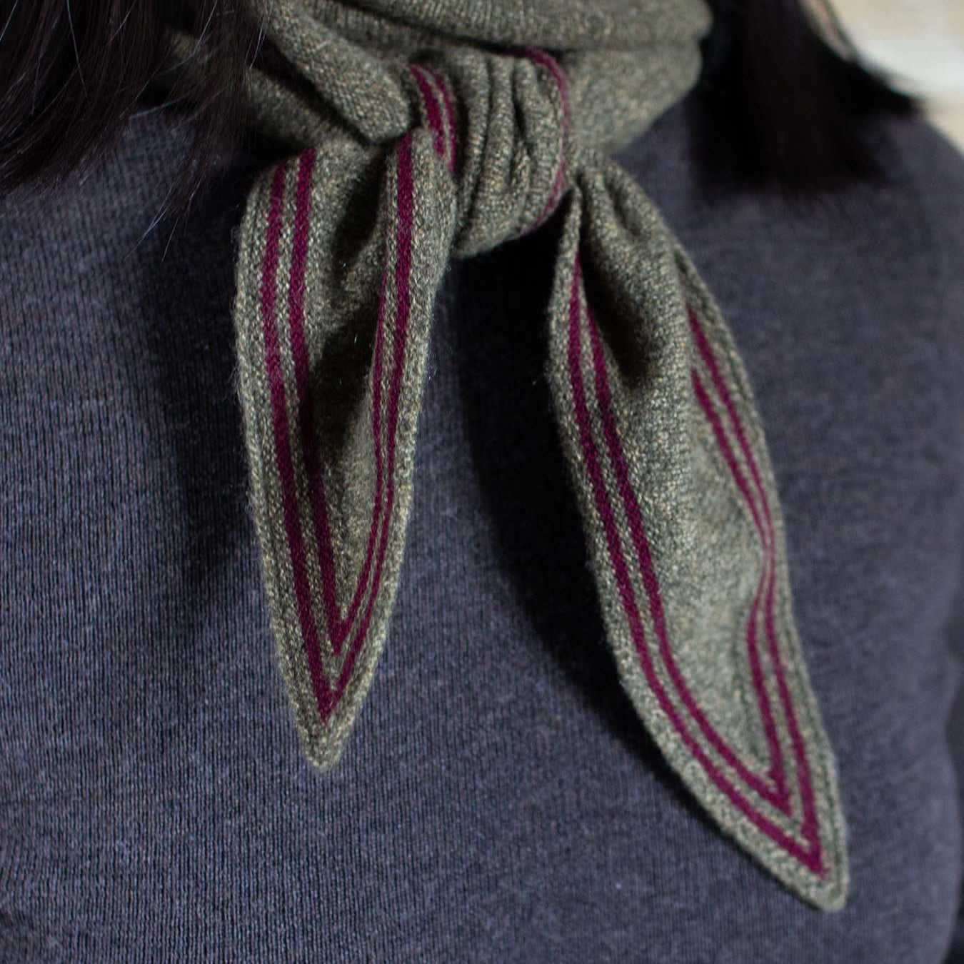 Green scarf with red stripes worn around the neck on a dark background