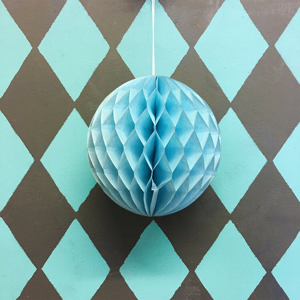 Light blue honeycomb paper ball hanging against a dark gray and light blue diamond patterned background.