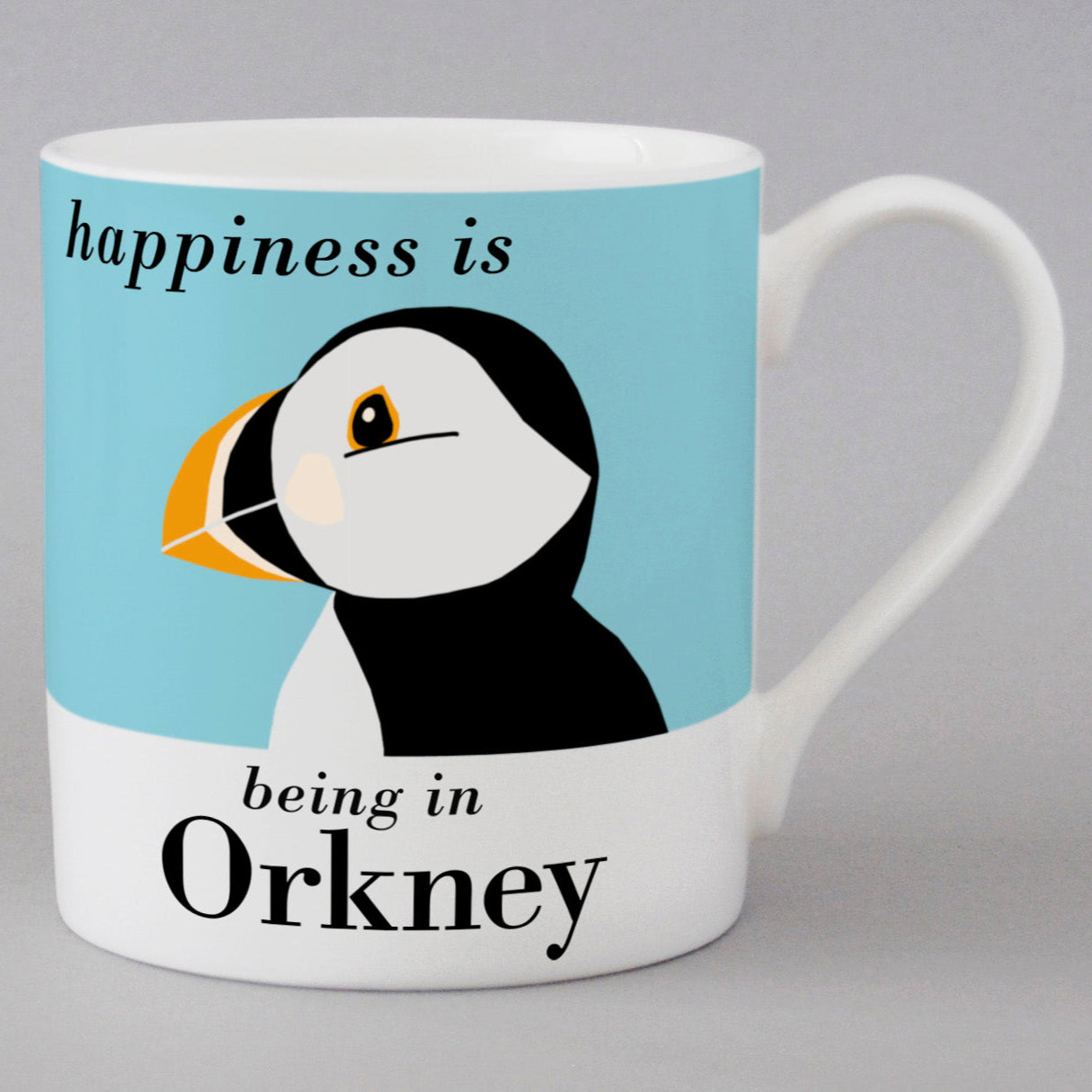 White mug featuring a stylized puffin illustration on a light blue background. Text reads "Happiness is being in Orkney".