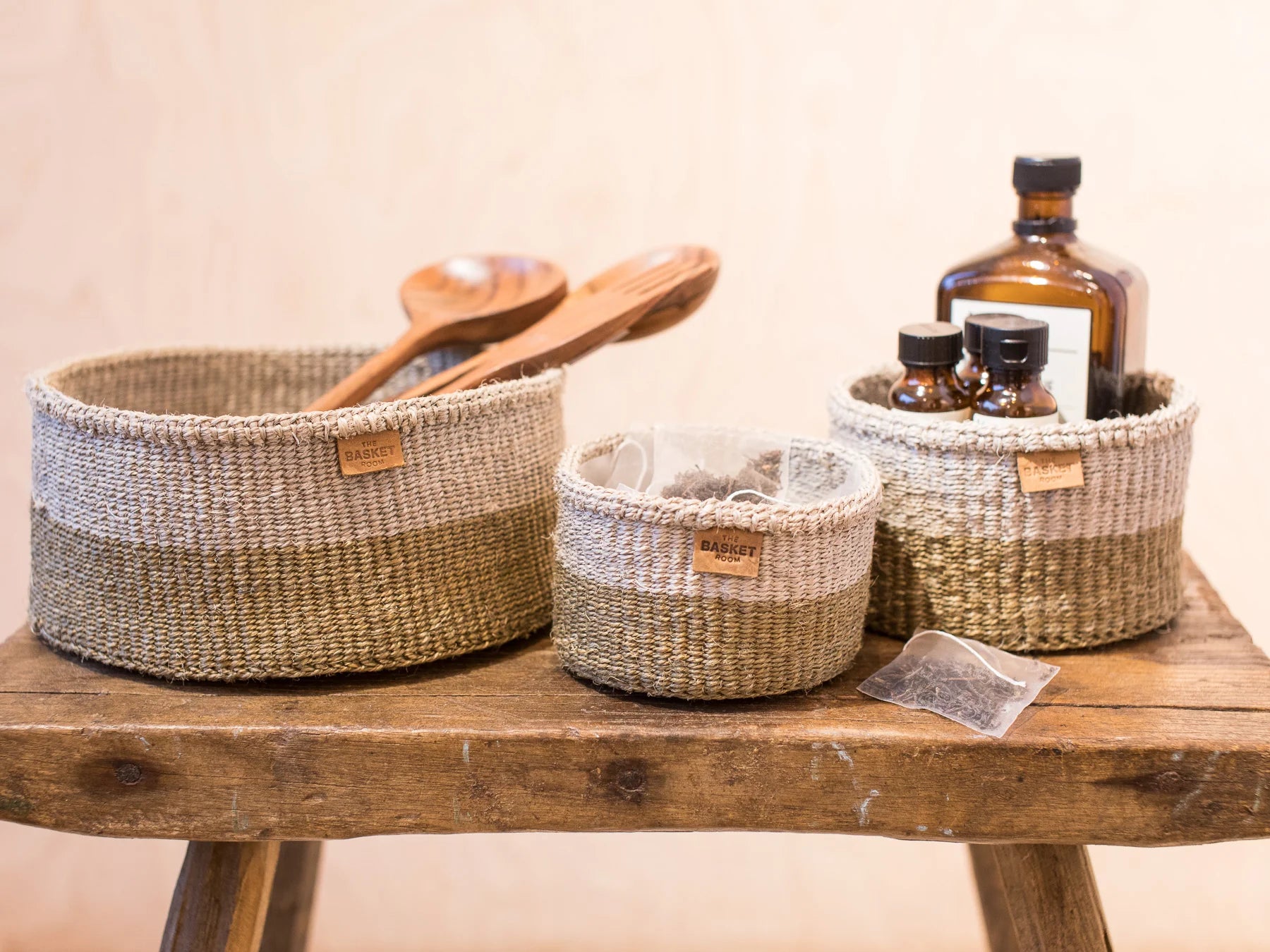 Three woven baskets, two-toned beige and brown, of varying sizes.  The largest contains wooden spoons.