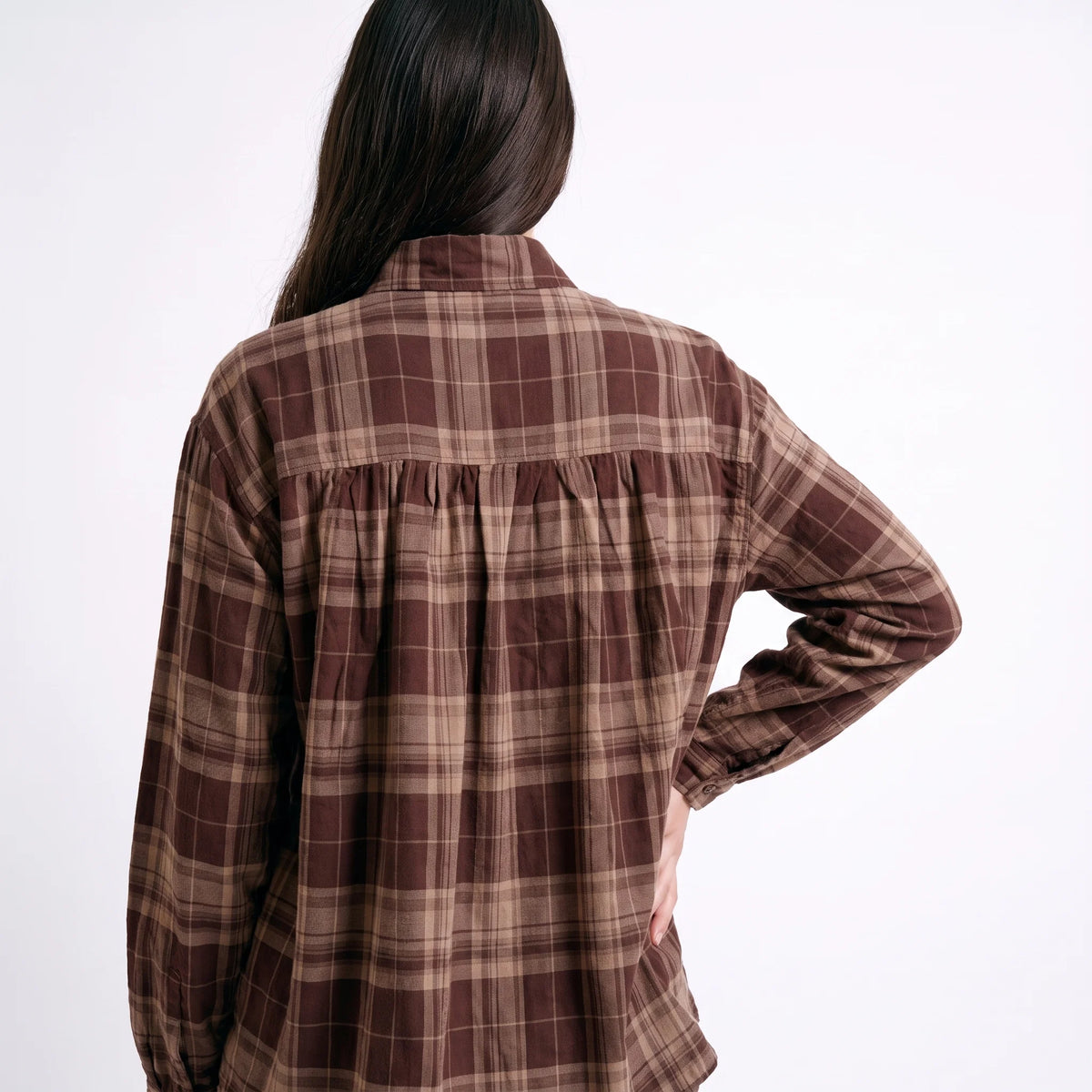 A woman shown from the back wearing a brown and beige plaid long-sleeve shirt with a gathered waist seam, against a plain white background.