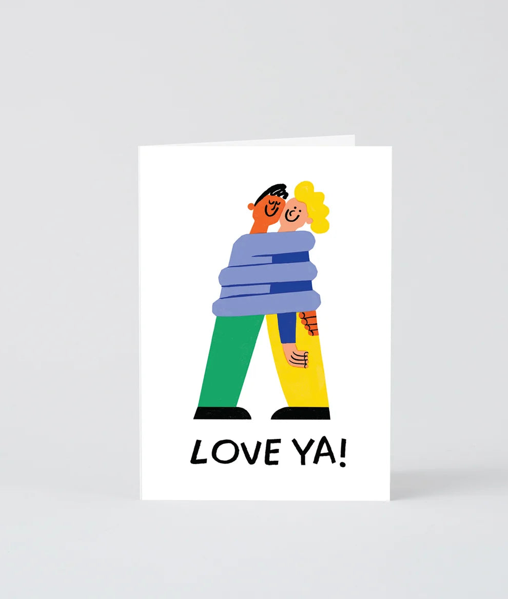 A white greeting card featuring a colorful cartoon illustration of a couple embracing, with the text 'LOVE YA!' printed in black at the bottom, shown against a light gray background.