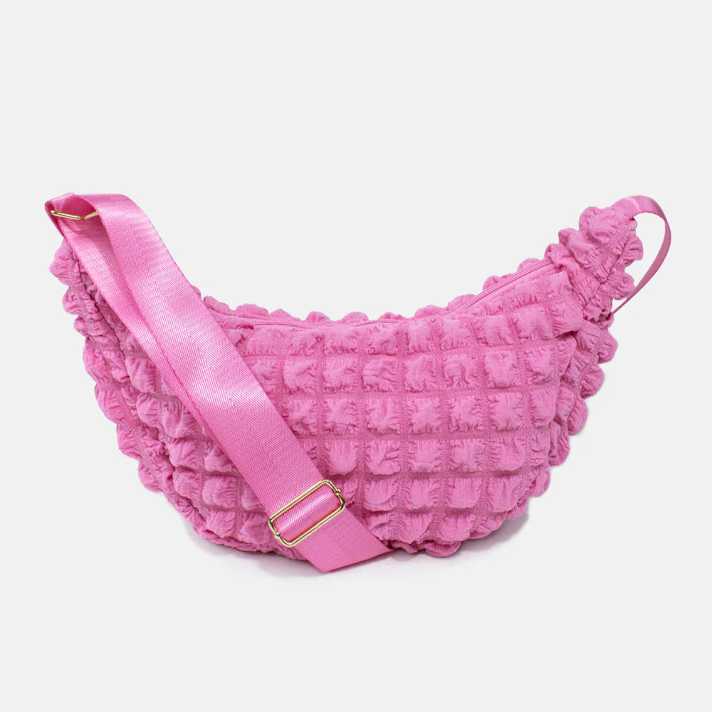 Pink textured crossbody bag with a curved shape and adjustable strap.