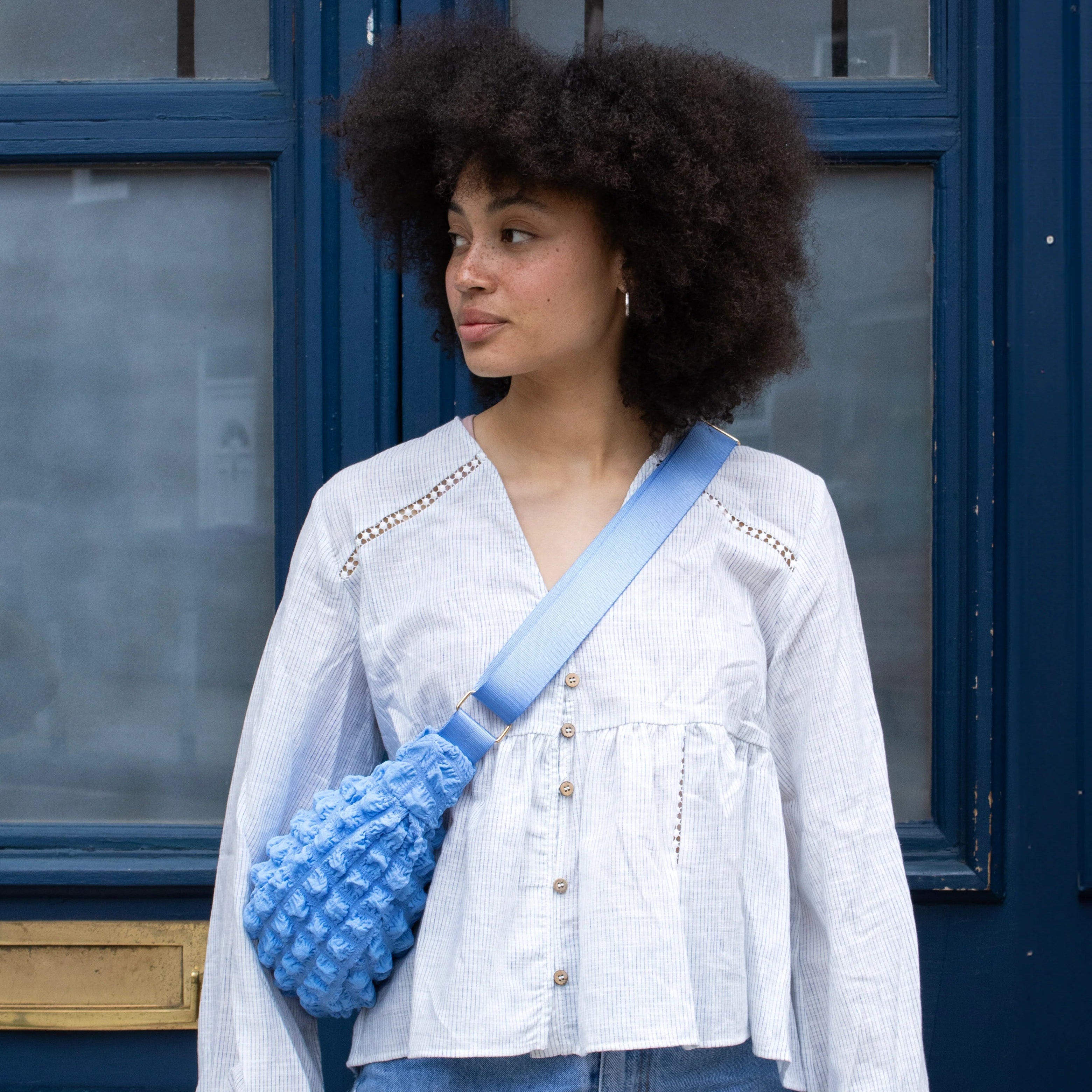 Light blue textured crossbody bag with a light blue strap, worn by a person with an afro.