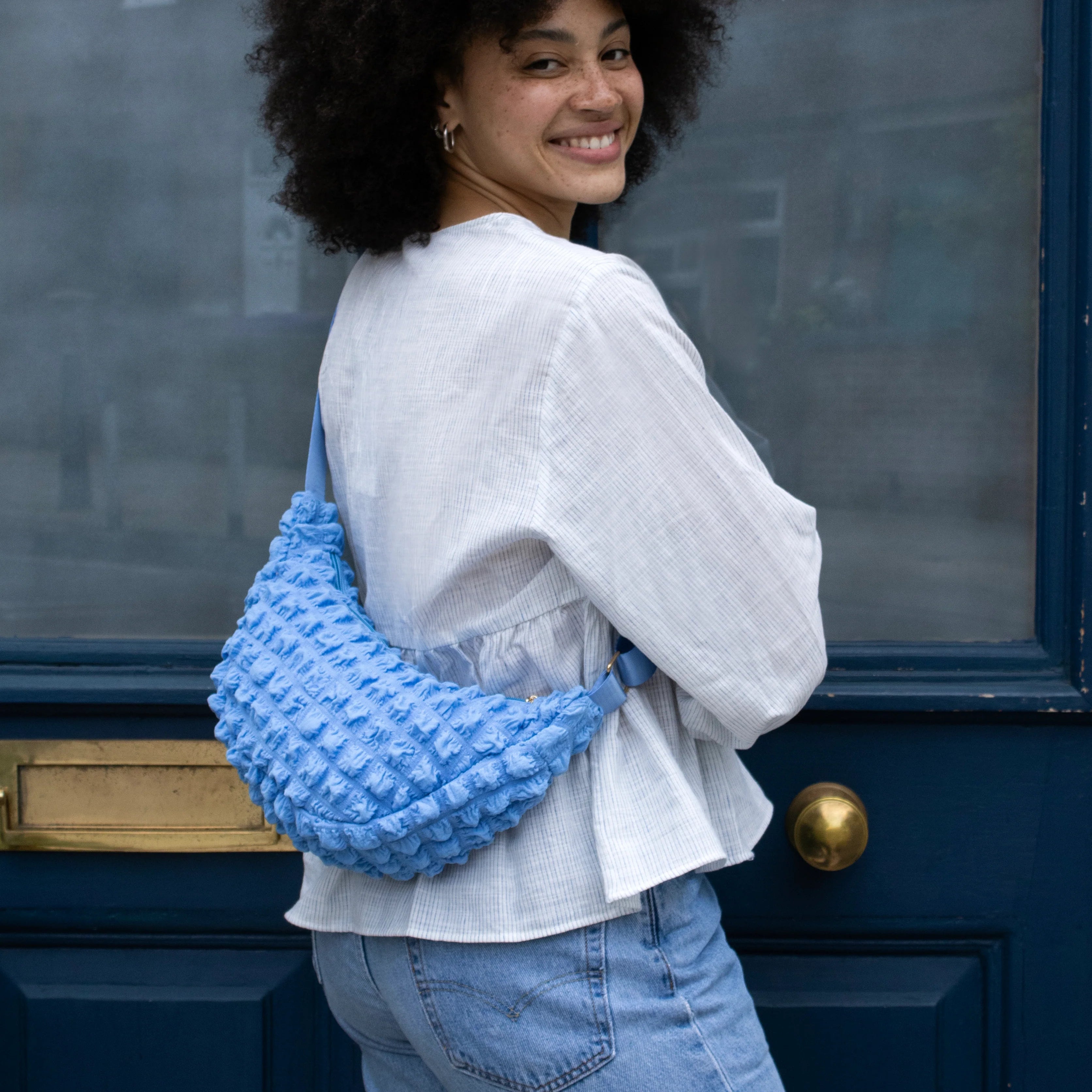 Textured light blue crescent-shaped crossbody bag with a short strap.