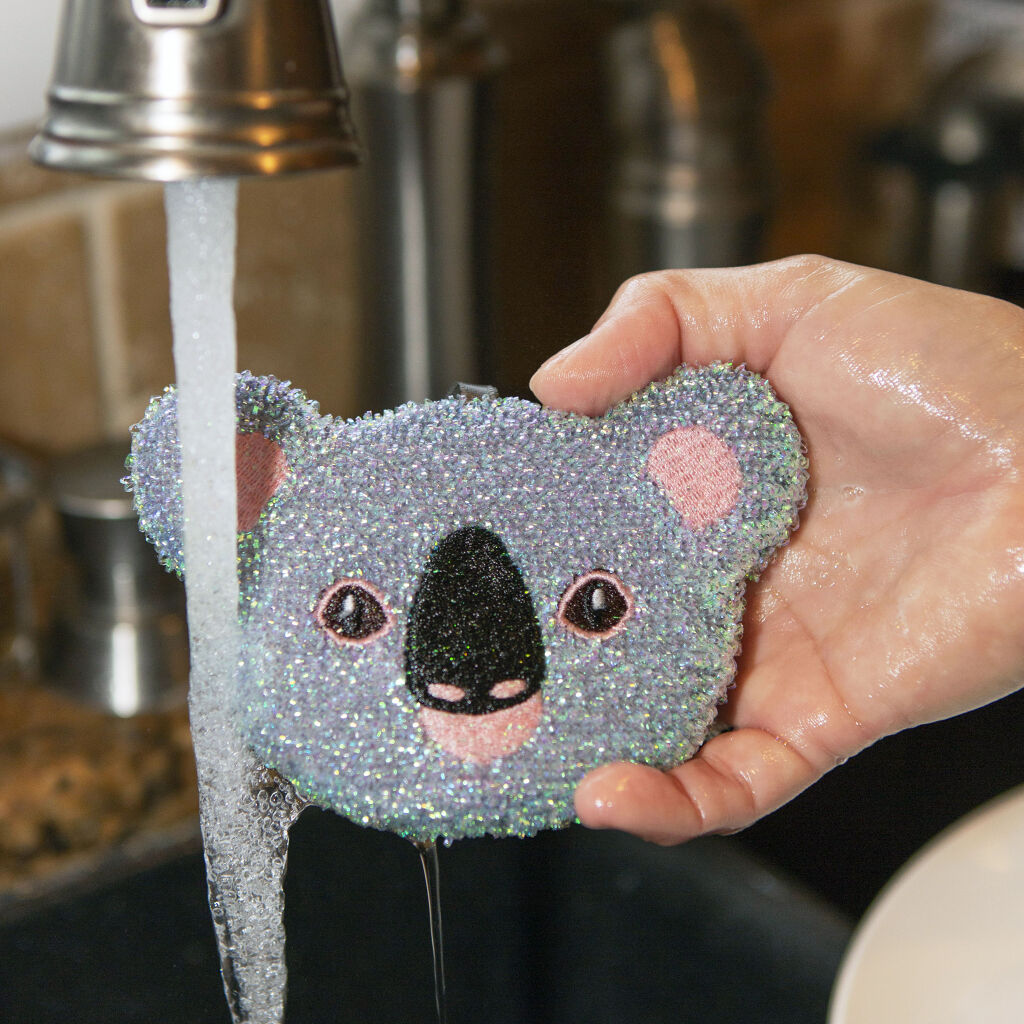 Glittery koala-shaped sponge being rinsed under a faucet.