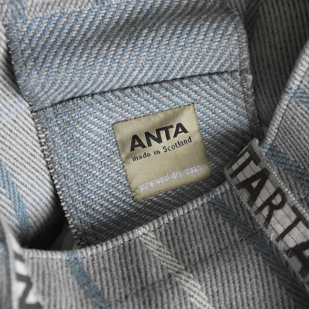 Close-up of a gray and blue herringbone pure wool Anta label sewn into a garment; made in Scotland, dry clean only.
