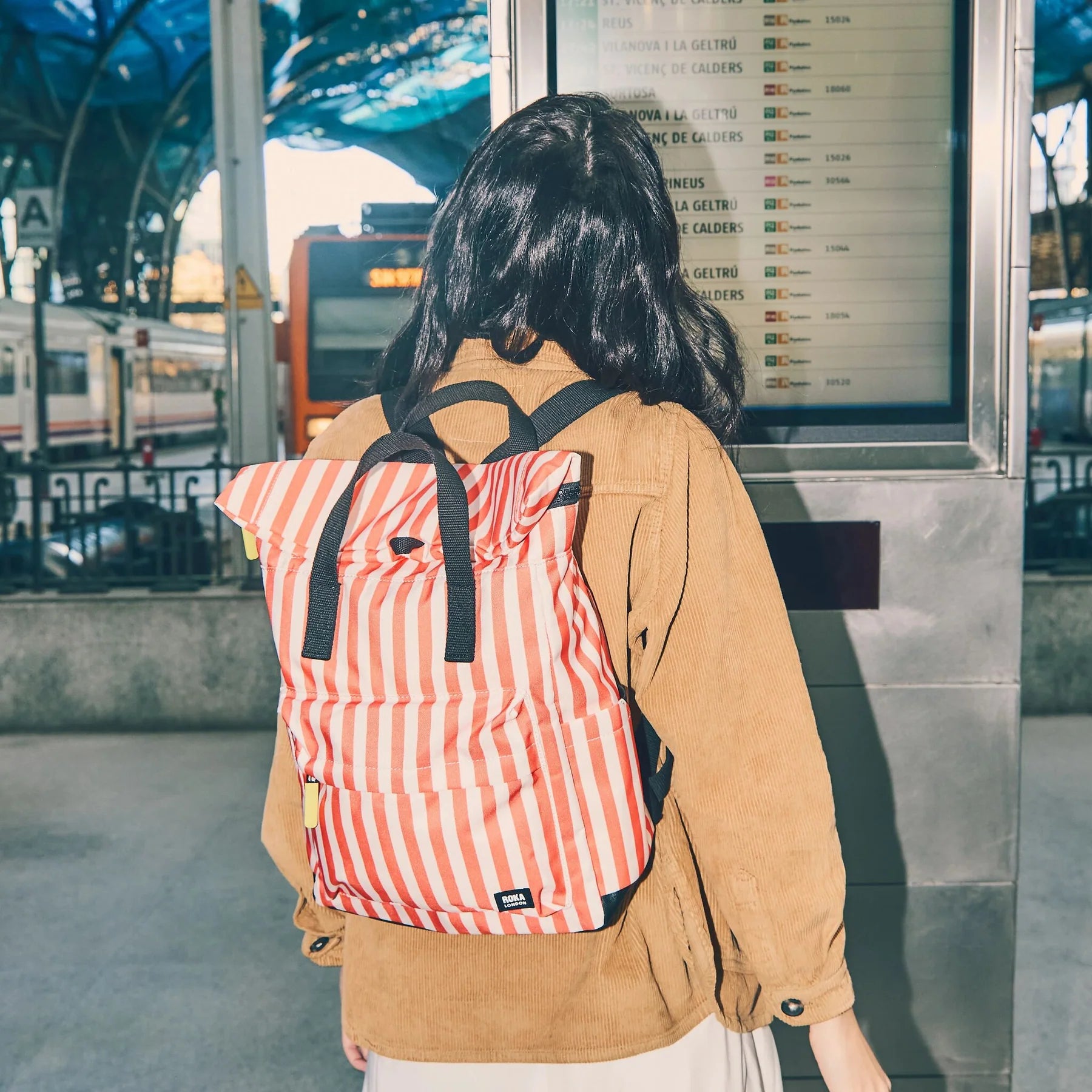Person with a red and white striped backpack standing in a train station.