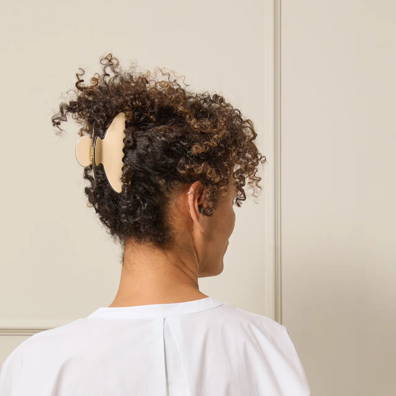 Person with curly hair wearing a beige hair accessory against a neutral background