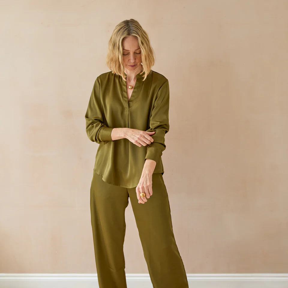 Woman wearing an olive green outfit standing against a beige wall.