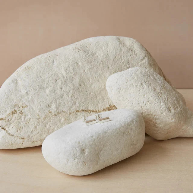 Pair of silver bar stud earrings resting on a light-colored stone.