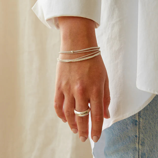 Silver ring and layered silver bracelets on a wrist.