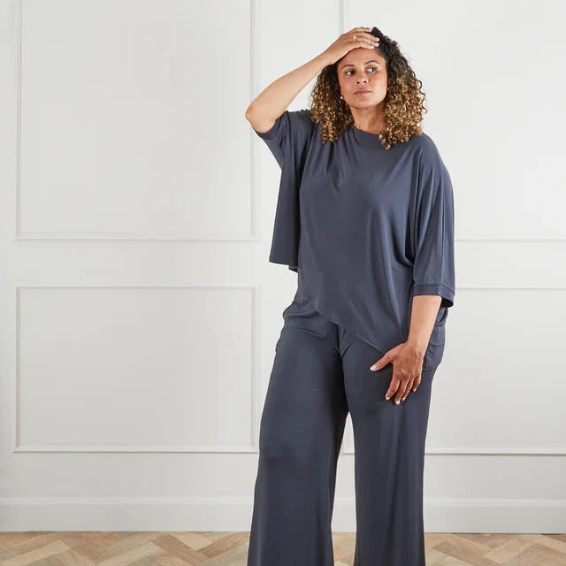 Model wearing Chalk UK in dark gray relaxed top and matching wide-leg pants, posing with a hand on her forehead.
