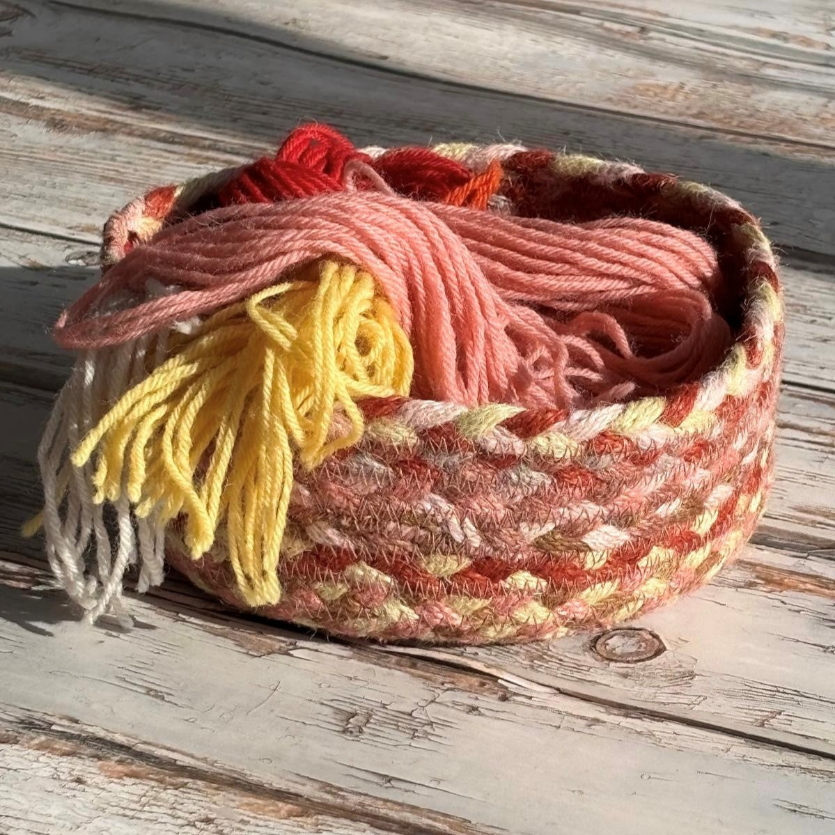 Round woven basket filled with pastel-colored yarn including pink, yellow, and red.