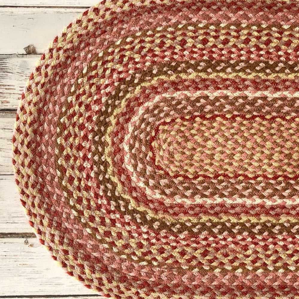 Oval braided rug in shades of pink, red, and brown.