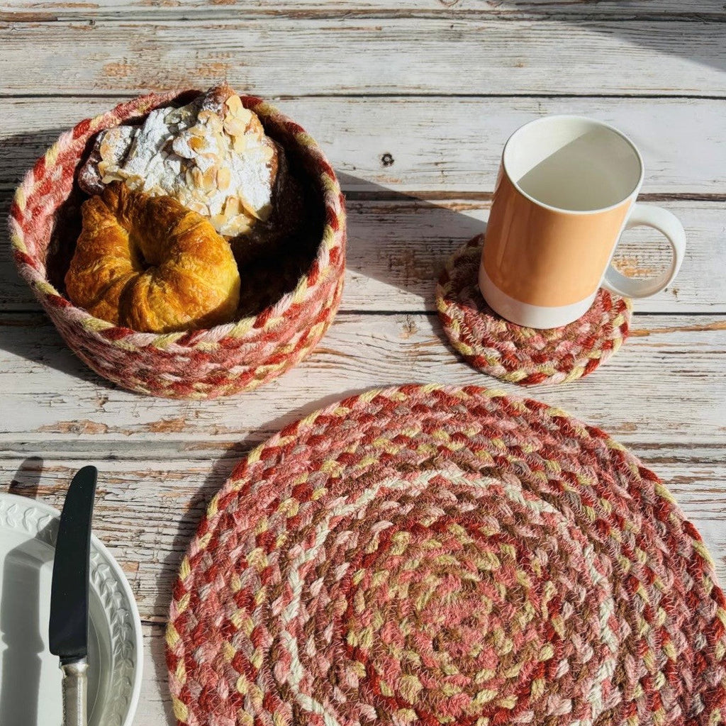 Round jute placemat in shades of red, pink, and beige; matching coaster and bread basket.