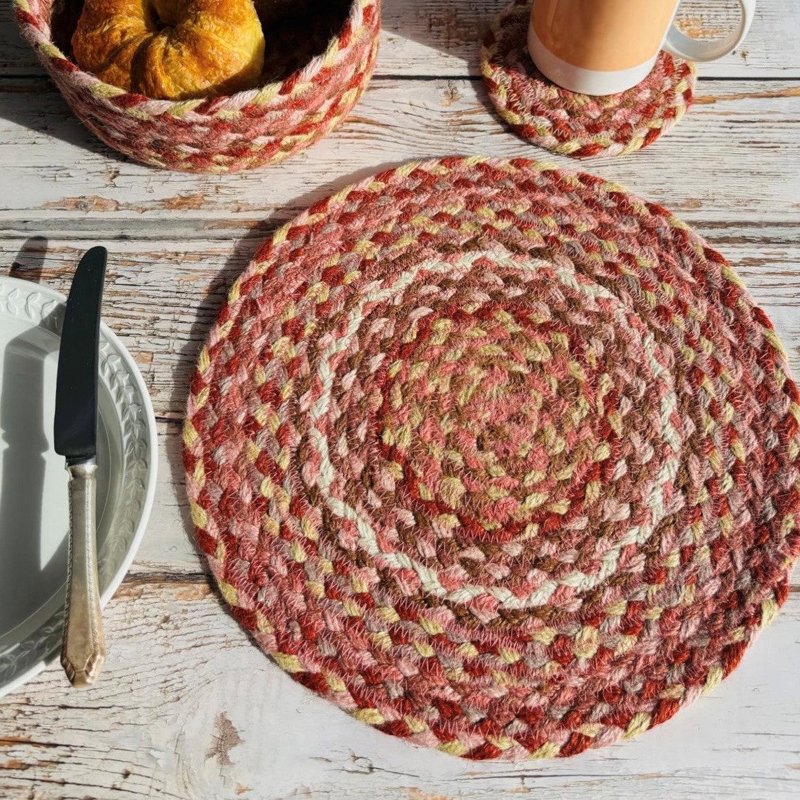Round braided jute placemat in shades of red, pink, beige, and brown.