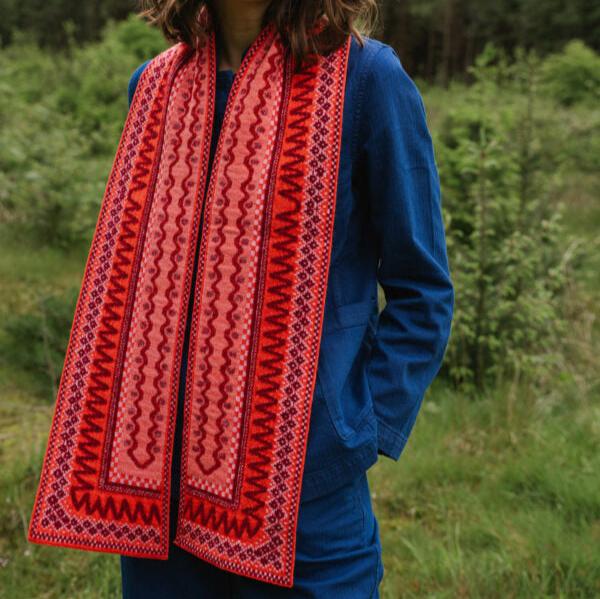 Long red and pink patterned wool scarf with intricate embroidered border.