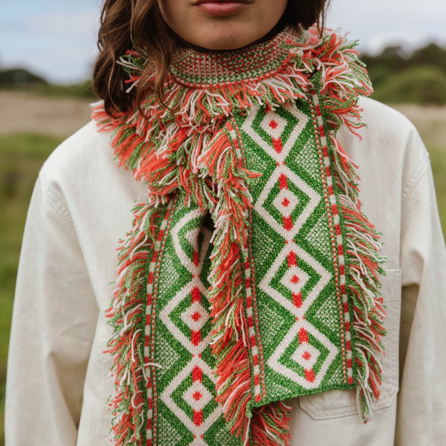 Green and coral fringed knit scarf with geometric pattern.