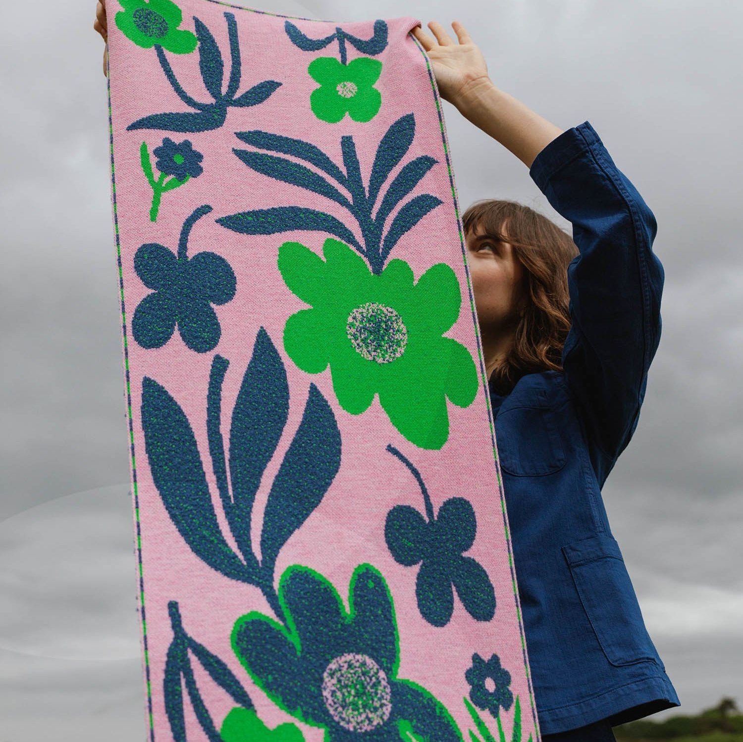 Pink knitted throw blanket with a bold floral pattern in shades of green and navy blue.
