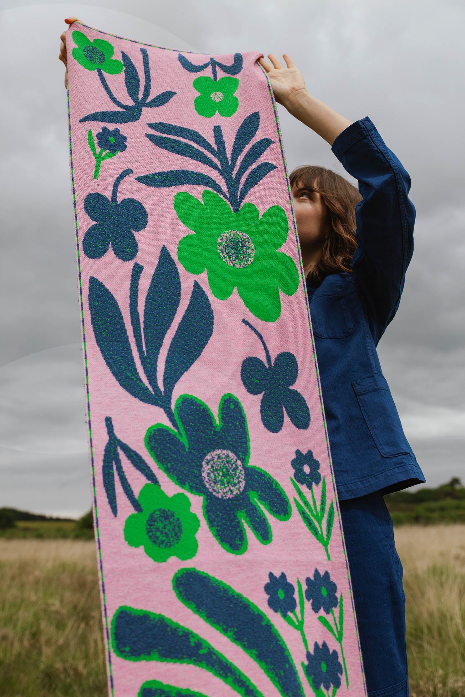 Pink knitted textile with a bold floral pattern in green and navy blue.