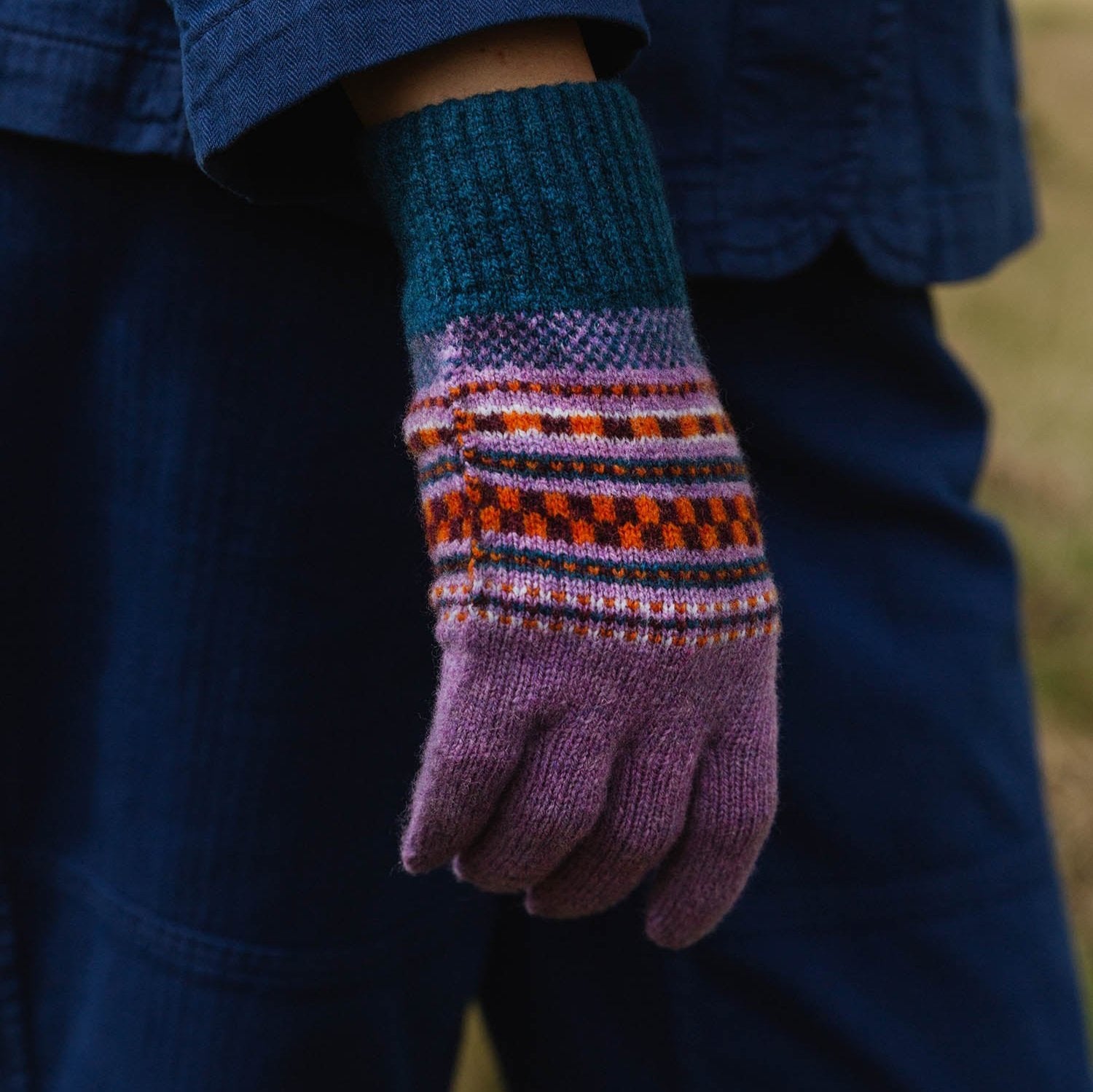 Purple knitted gloves with teal and orange patterned cuffs.