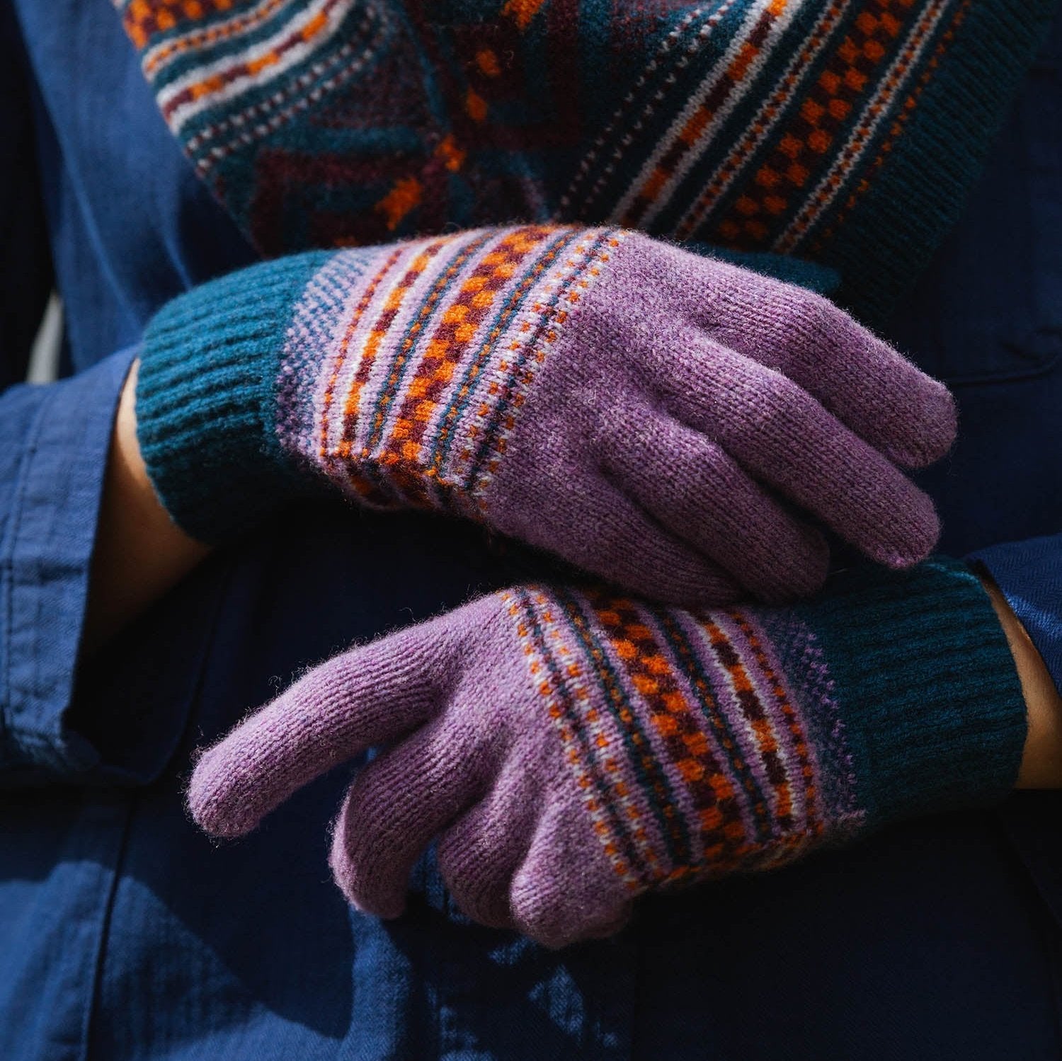 Pair of purple knitted gloves with teal cuffs and orange, maroon, and white Fair Isle pattern.