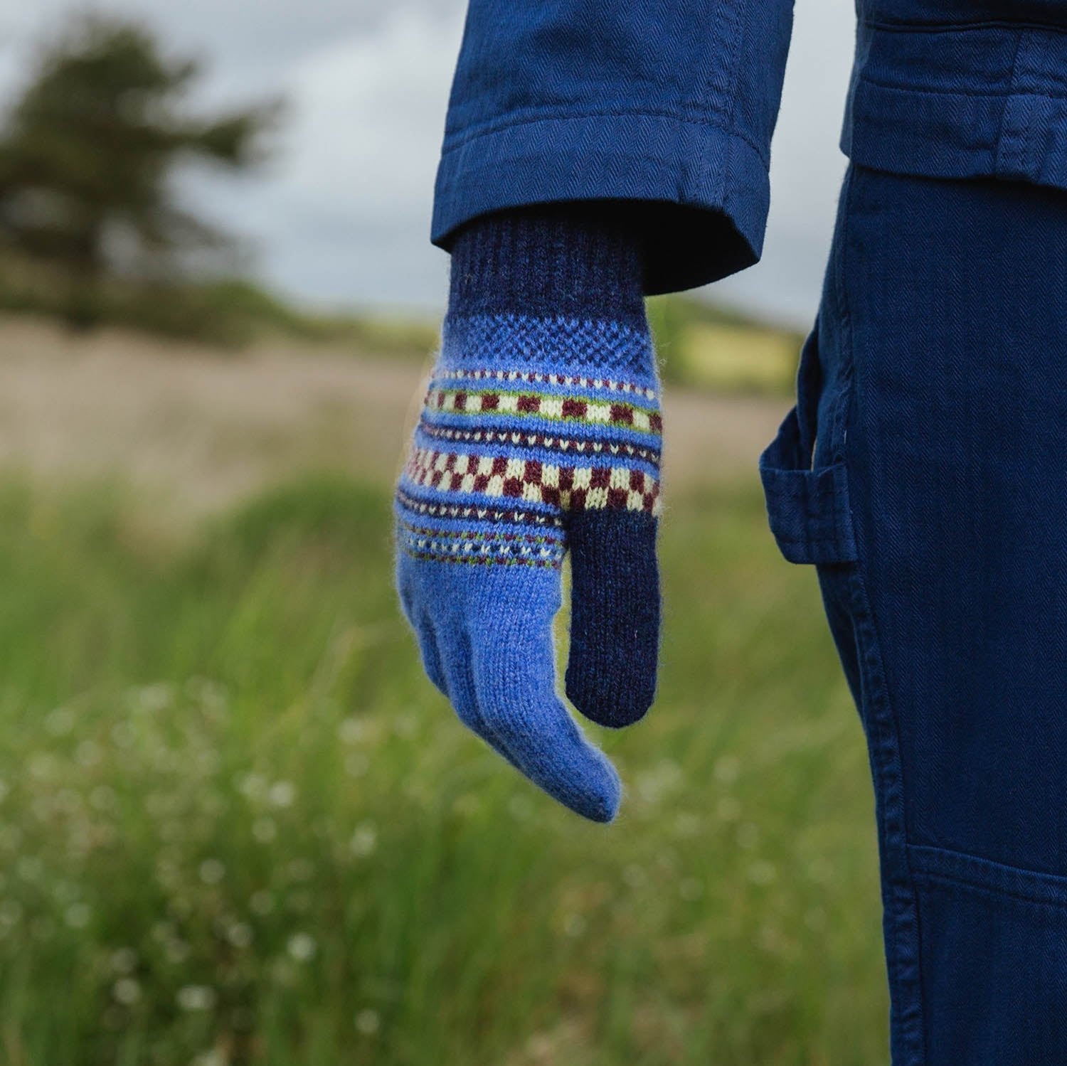 Blue knitted glove with a patterned cuff featuring stripes and checks.