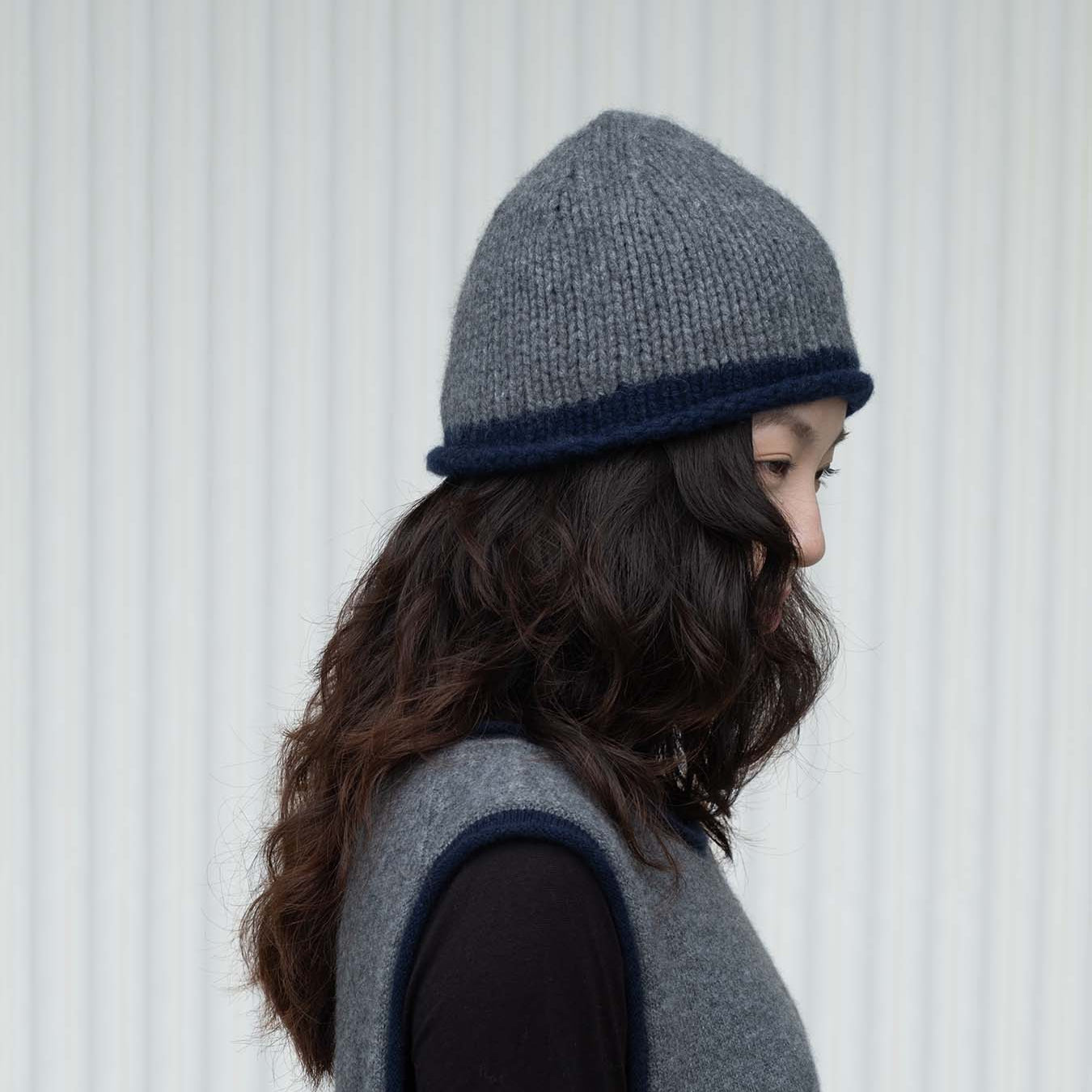 Person wearing a gray knit beanie and gray vest against a white background