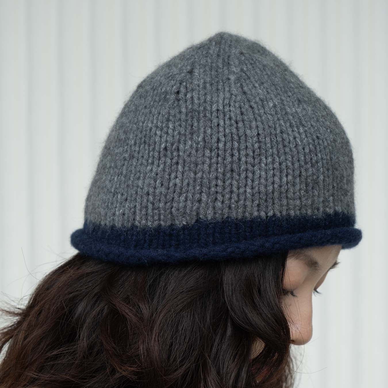 Person wearing a gray knit beanie with a blue rim against a white background