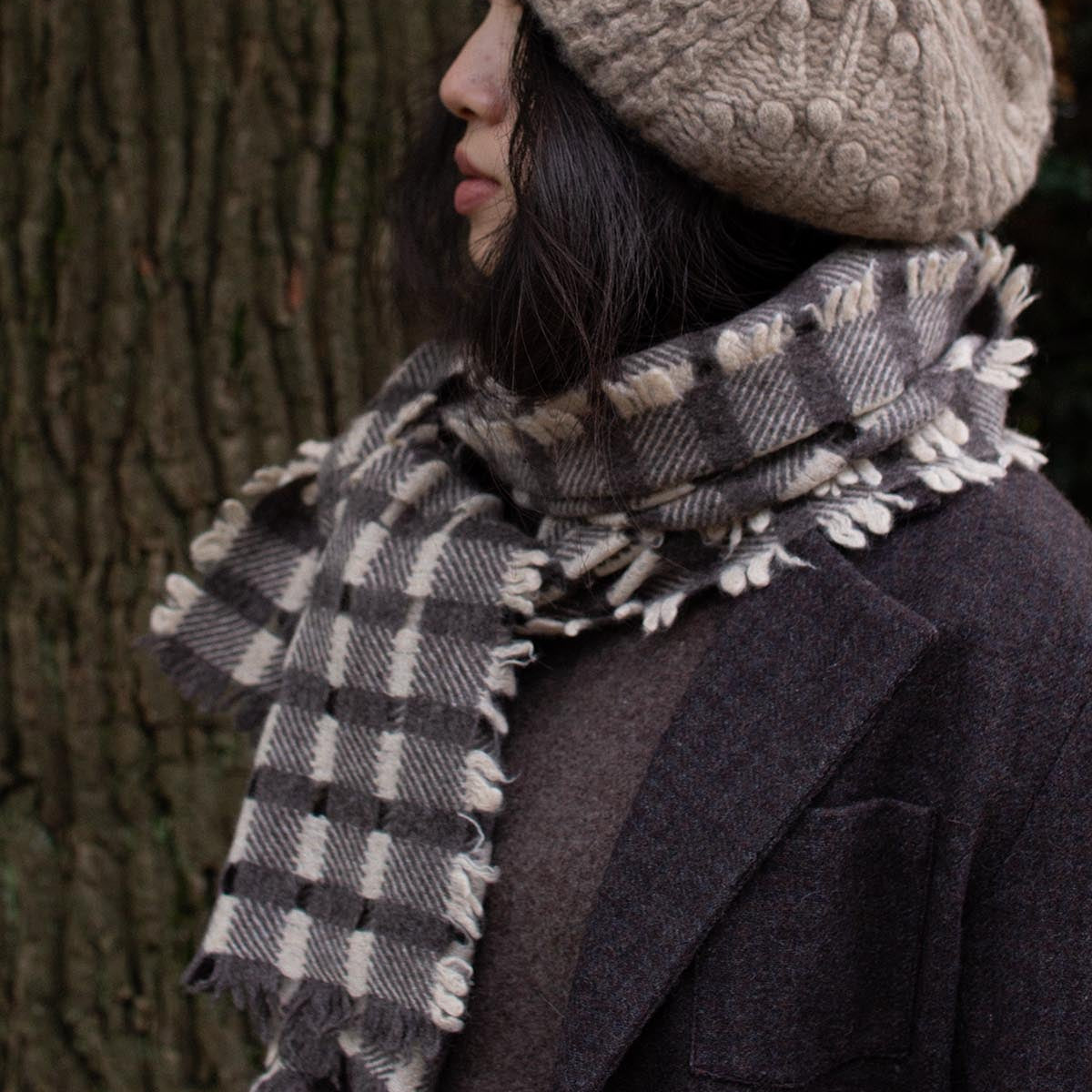Person wearing a patterned knit hat and plaid scarf against a tree background