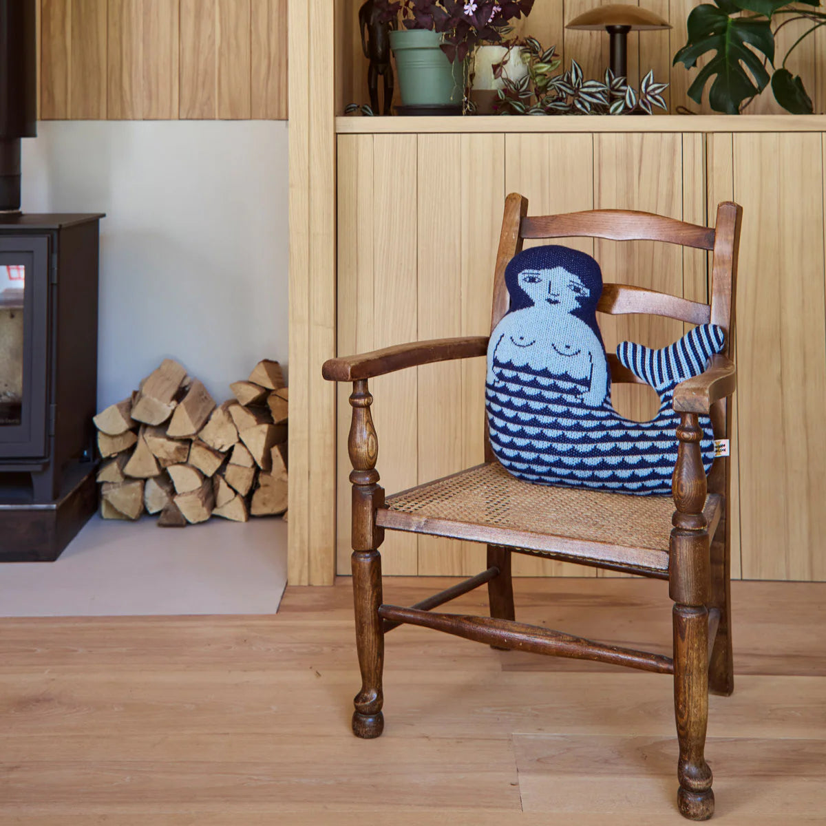 Wooden chair with a decorative cushion featuring a mermaid design in a room with wooden walls and a fireplace.