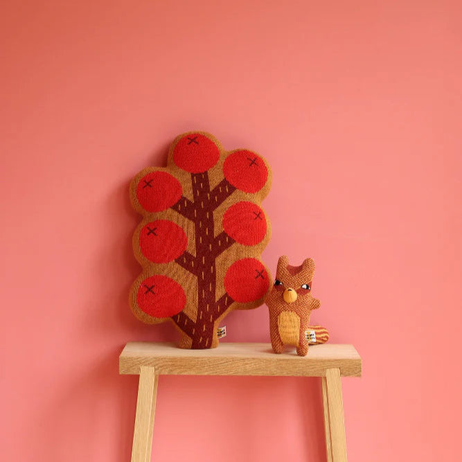 Stuffed toy squirrel and tree with red apples on a pink background