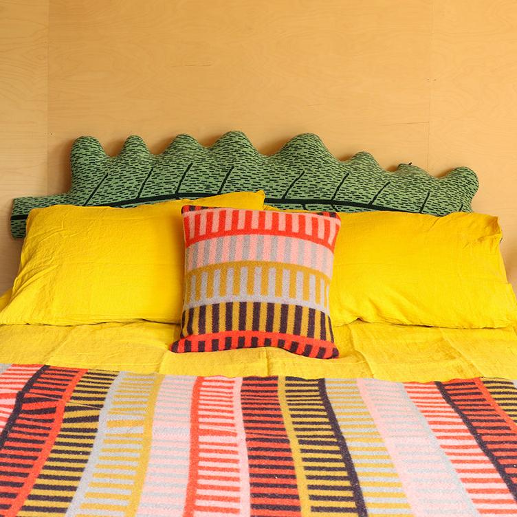 Bright yellow bedding with a green leaf-shaped headboard, featuring a striped pillow by Donna Wilson.