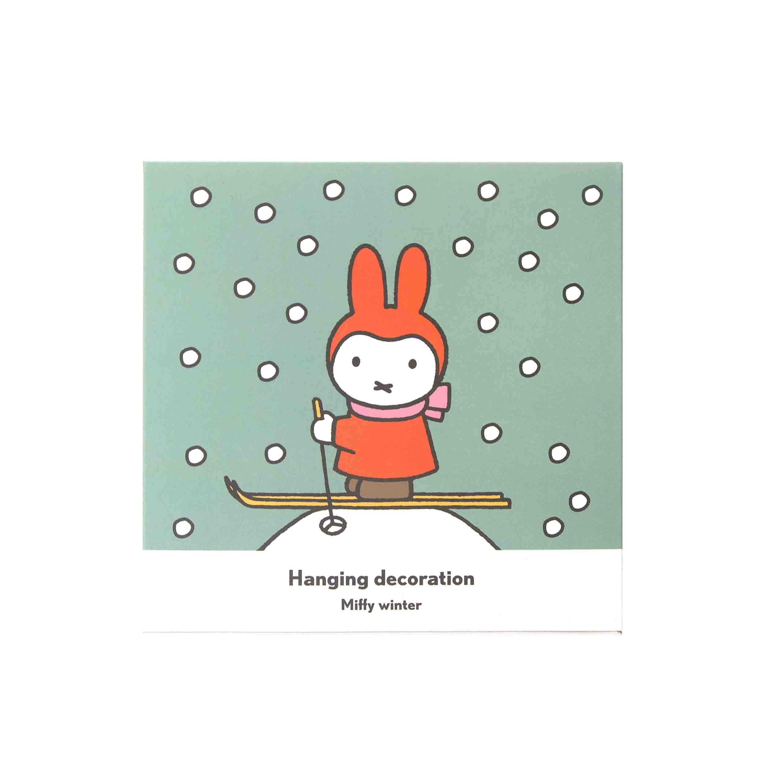 Miffy winter hanging decoration; illustration of Miffy in red ski outfit on skis against a teal background with white dots.