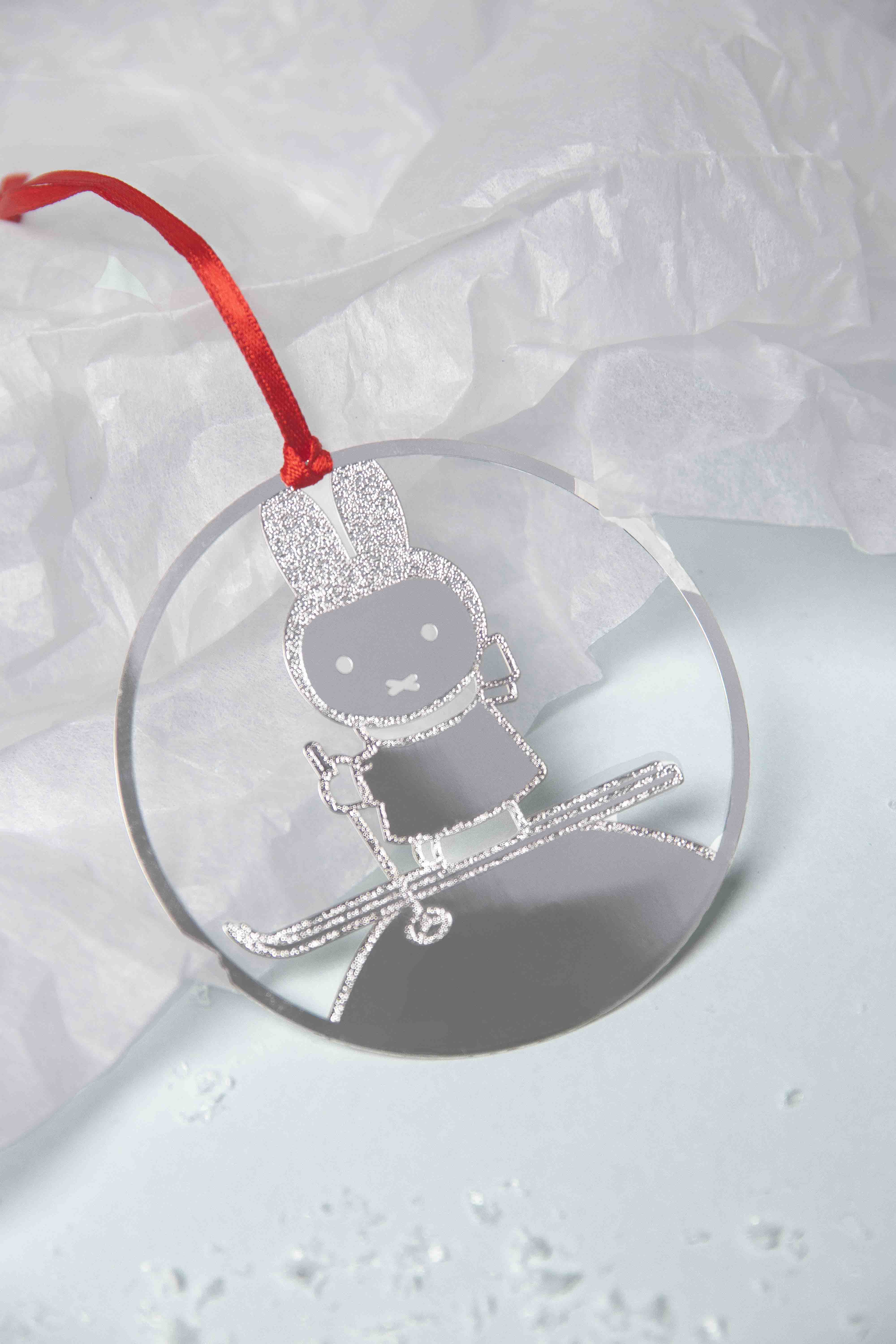 Silver glitter-textured bunny skiing ornament on a round, clear glass decoration.  Attached is a red ribbon.
