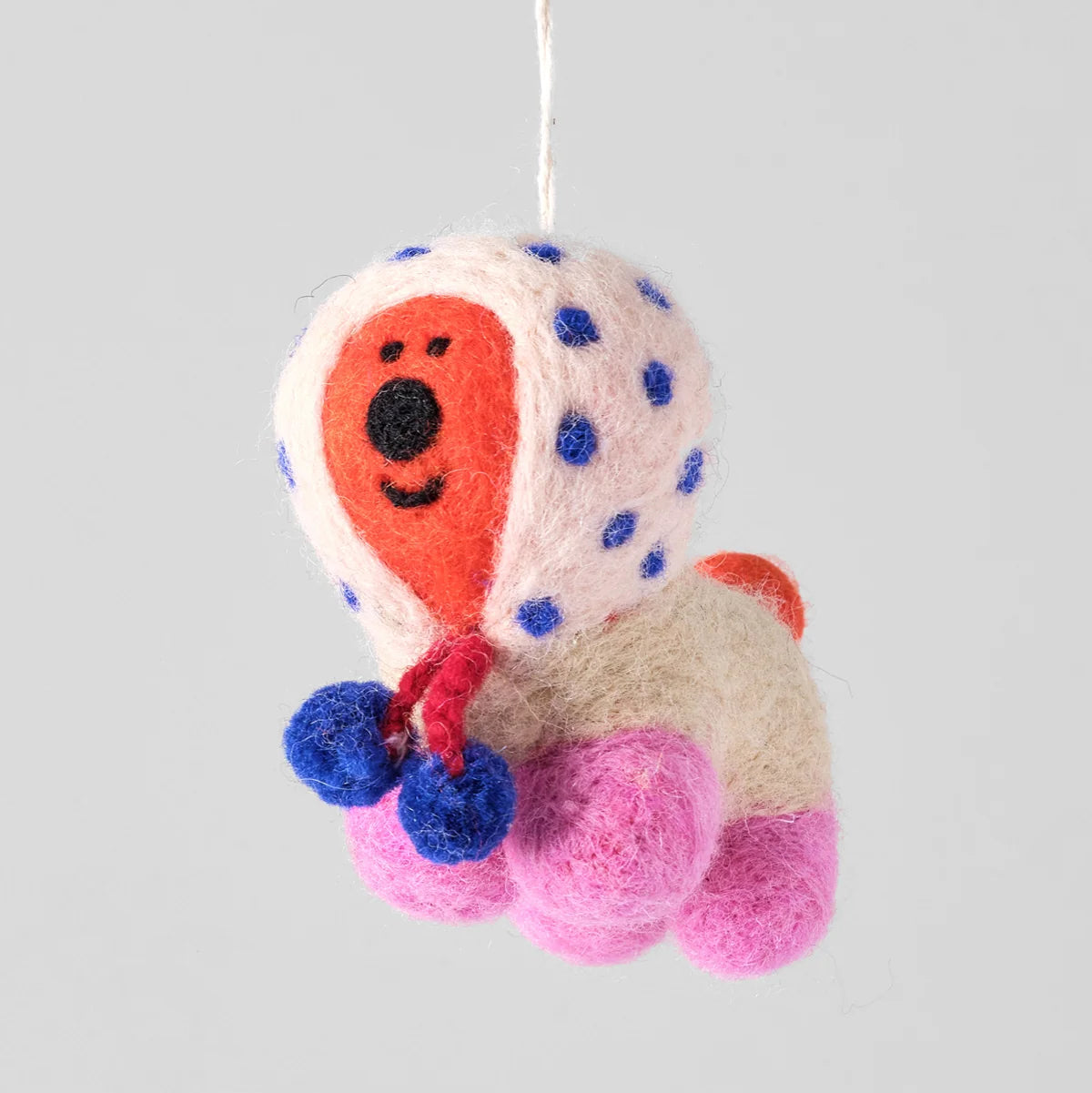 A hand-felted wool dog hanging ornament in a playful multicolor design with a cream-colored body, pink paws, blue polka dots, and an orange face.