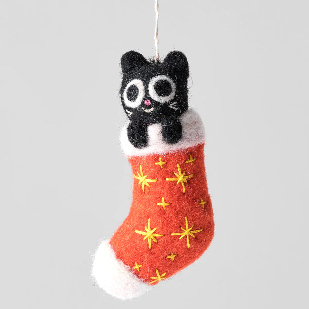 Black cat in a red stocking ornament with yellow stars on a gray background
