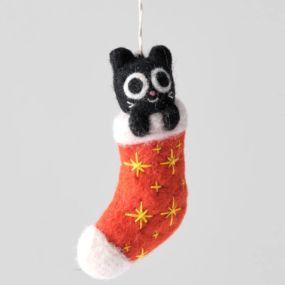 Felted black cat in a red stocking with yellow stars on a gray background