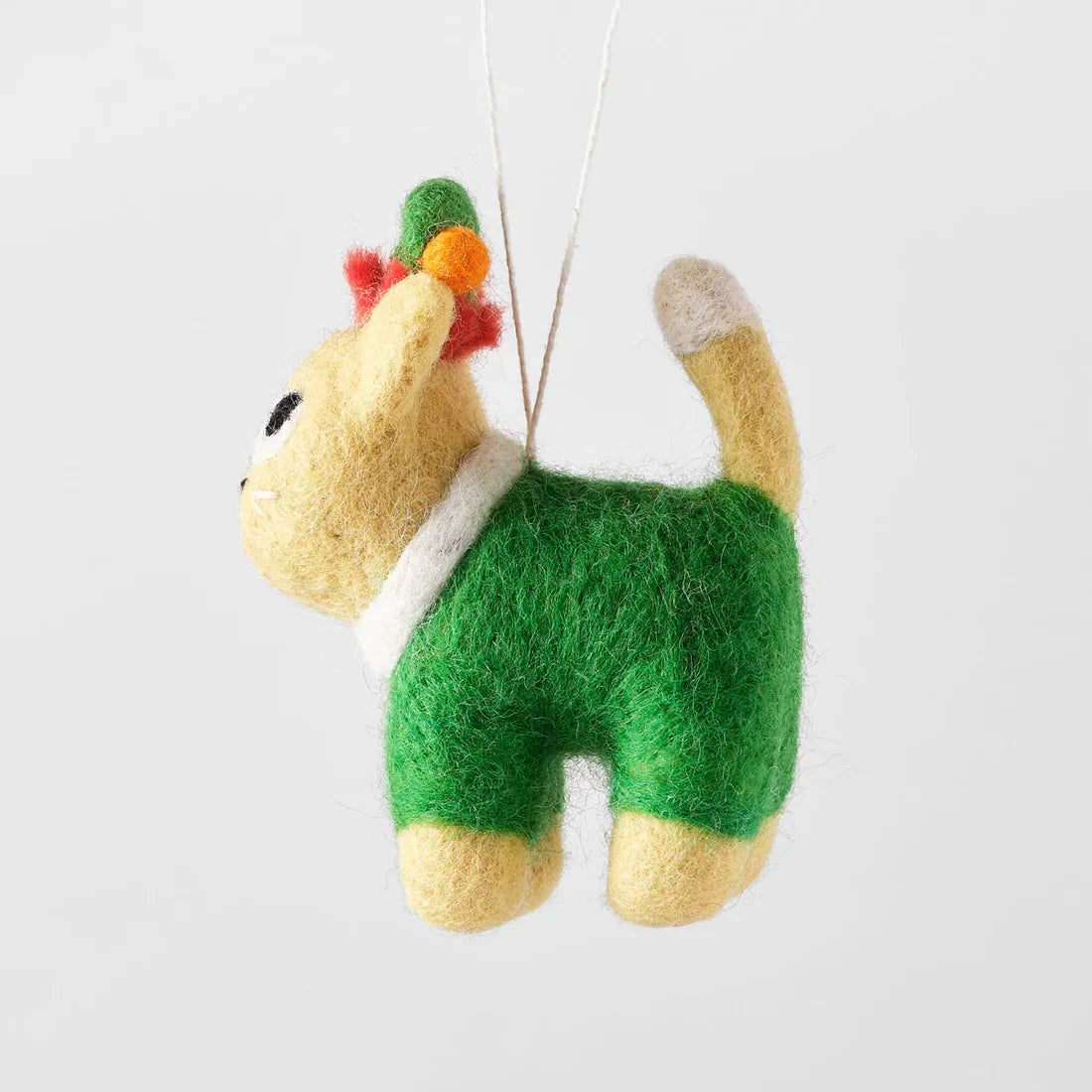 Needle-felted cat ornament; pale yellow body, green outfit, small multicolored headpiece, hanging from white string.