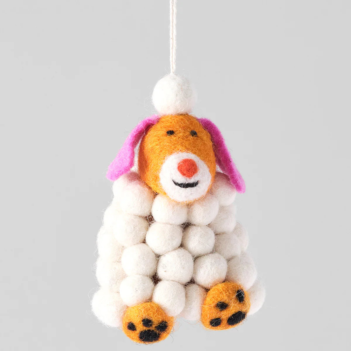 Decorative dog ornament made of white balls, orange felt, and pink ears on a gray background