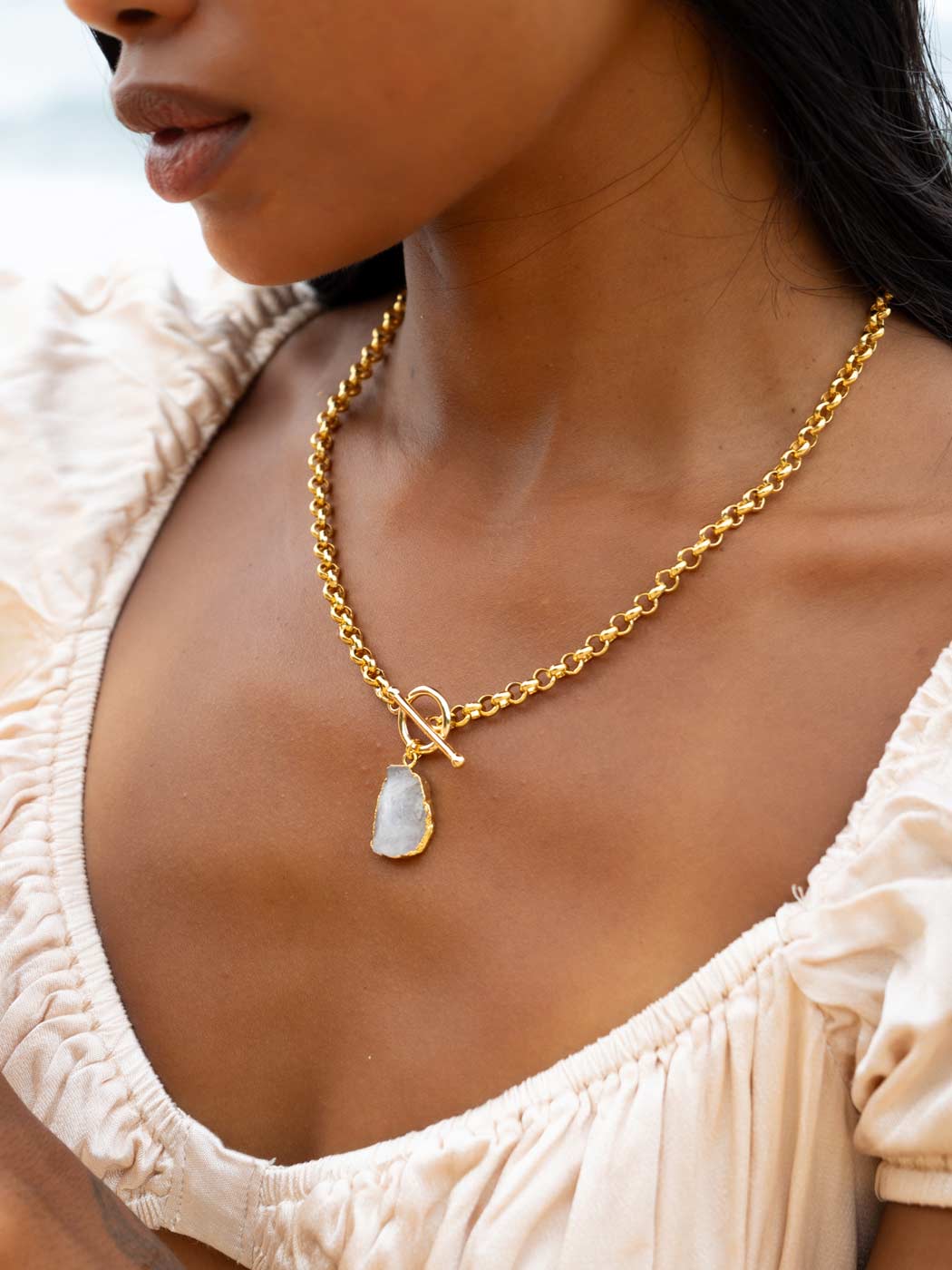 Gold necklace with a pendant worn by a person in a beige top.