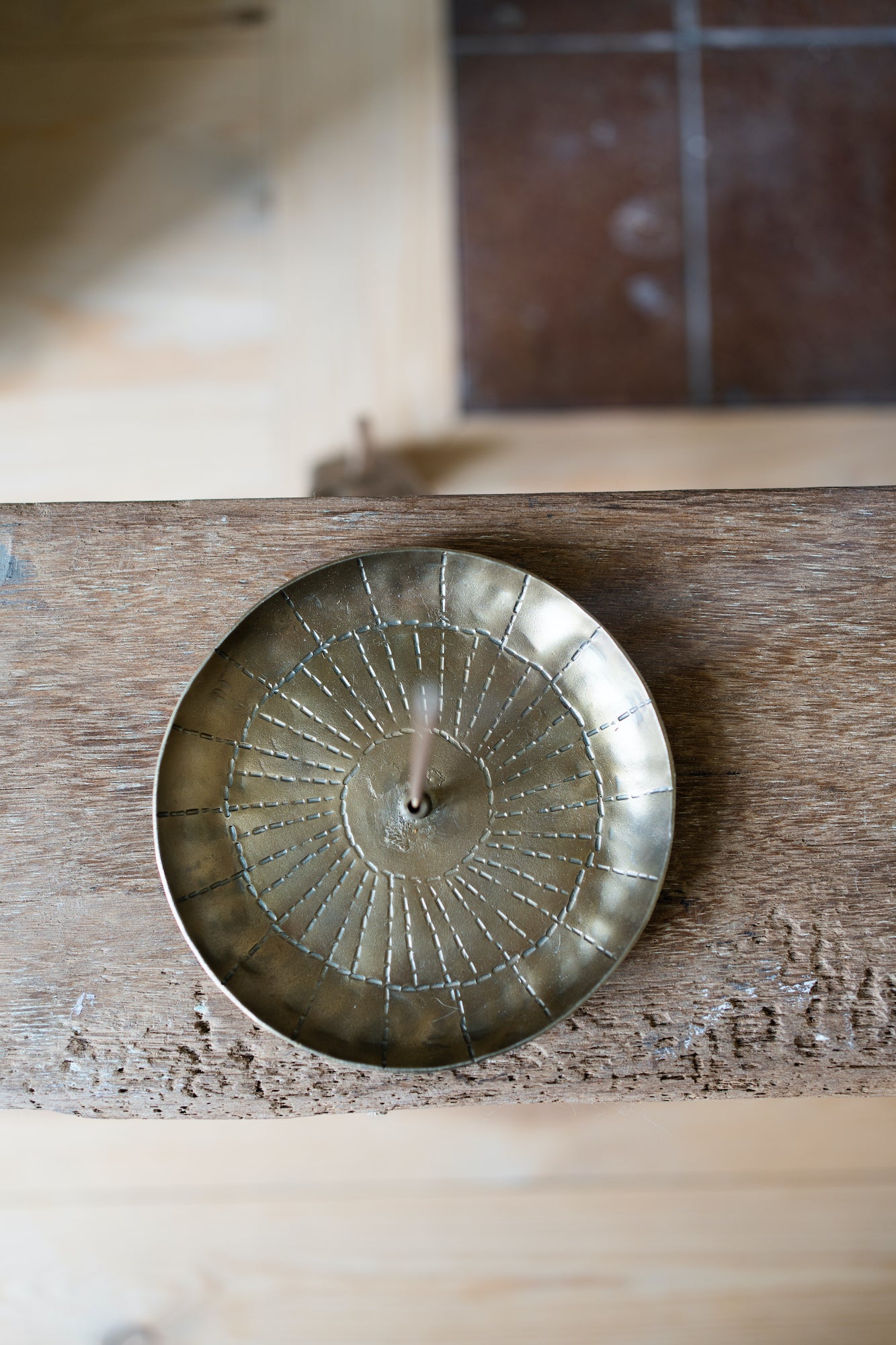 Brass incense holder with a sunburst design, holding a single incense stick.