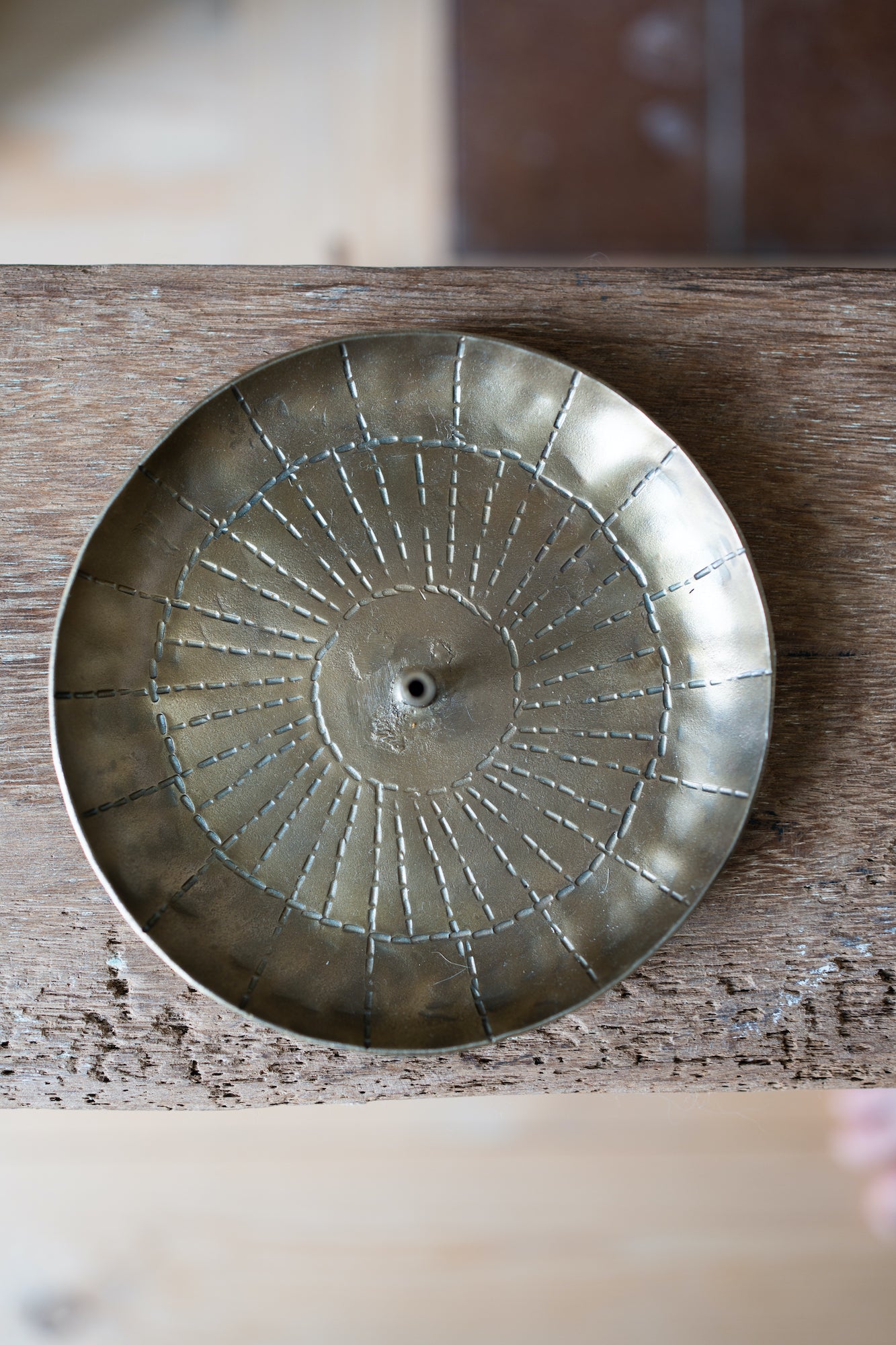 Brass incense holder with a circular, sunburst-patterned design.